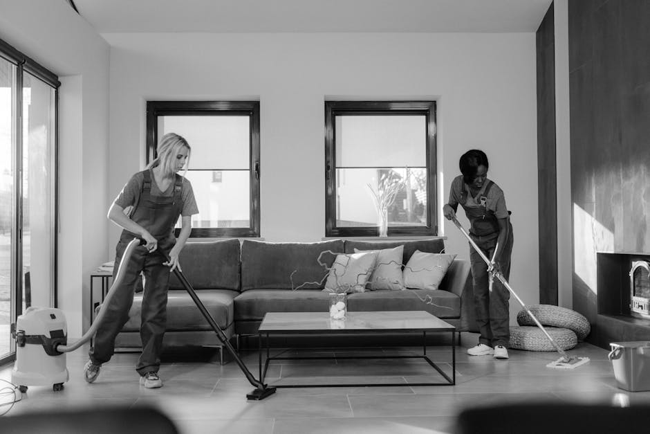 Three professional cleaners from Watford Cleaners are performing surface cleaning and deep cleaning in a modern living room. The room features a light-colored tiled floor with a shiny, well-maintained